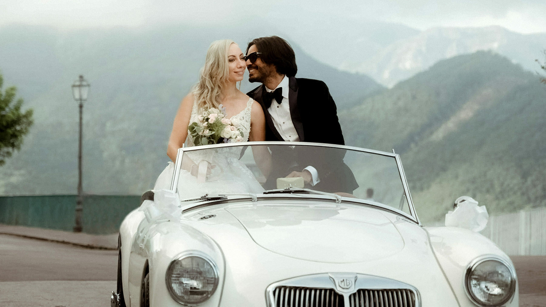 Wedding couple kissing on a vintage car in Ravello after their intimate wedding in Villa La Rondinaia