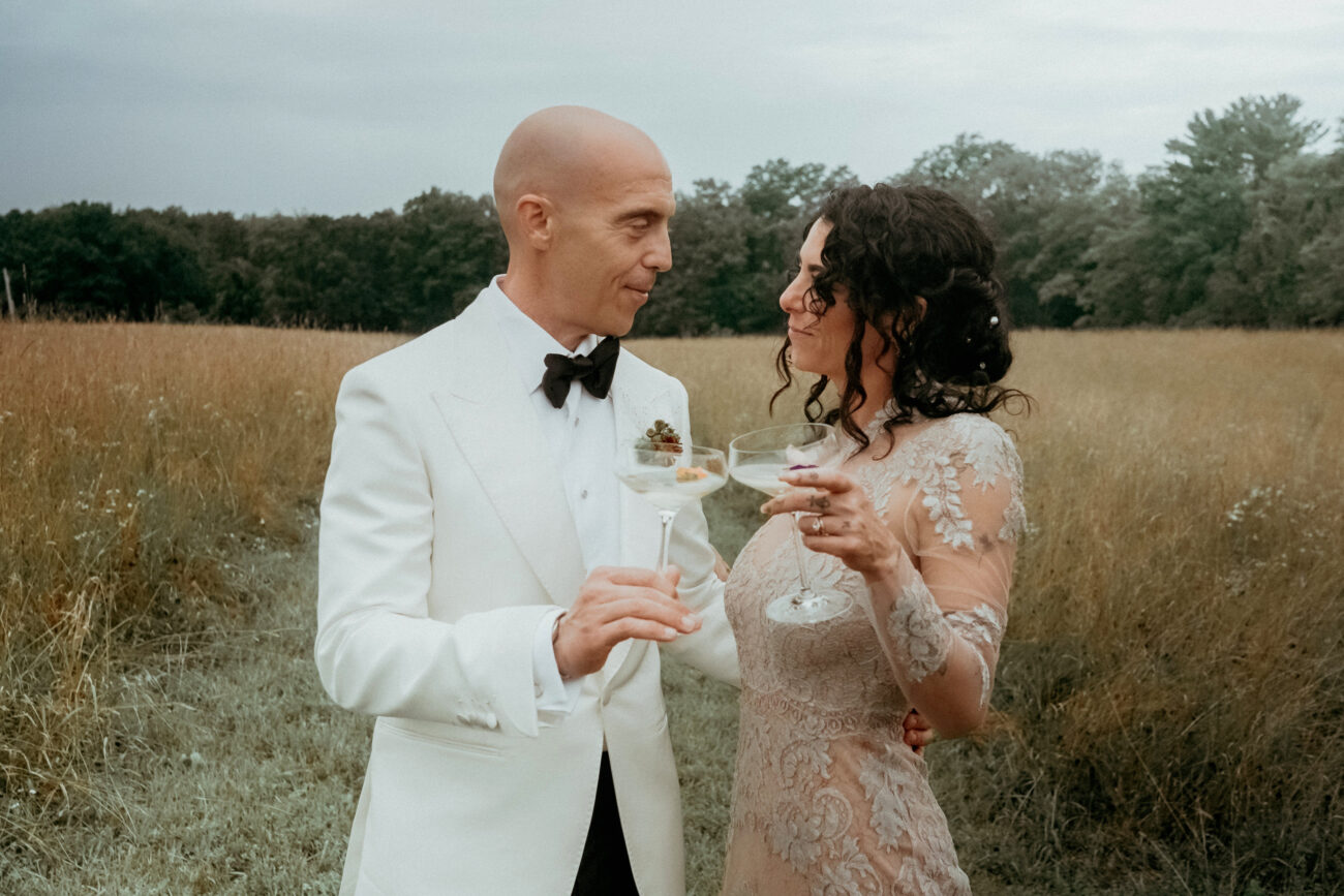 Couple in the fields of Gather Greene holding champagne glasses filmed by a New York Wedding Videographer
