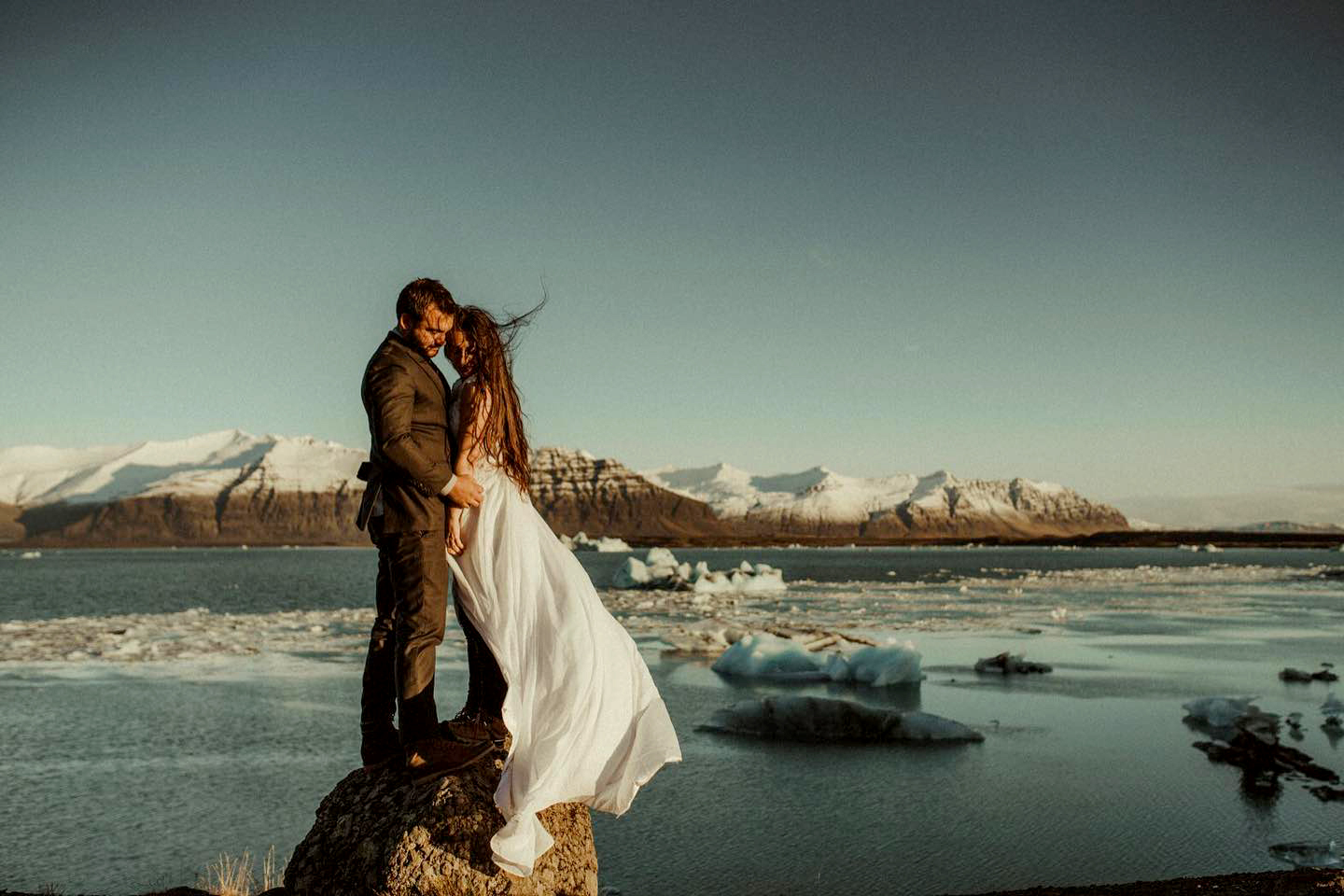 Iceland Elopement Videographer for Adventure & Intentional Celebrations 9 A couple in wedding attire hugging in front of the glacier lagoon, filmed by an Iceland Elopement Videographer