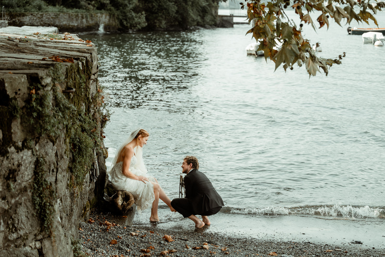 A groom washes the feet of his bride on the shore of the lake following a Christian ritual after their Lake Como Elopement in Villa Monastero