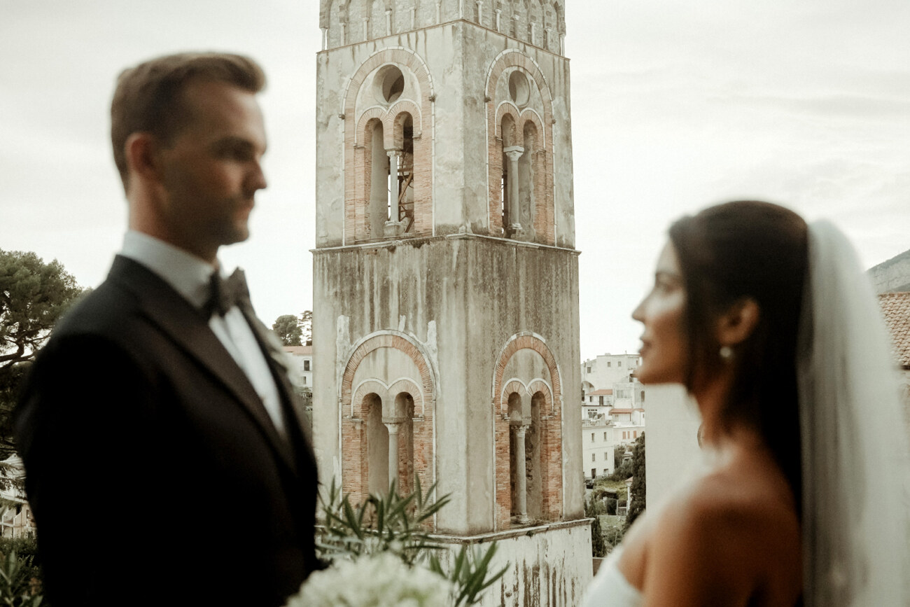 The bell tower of the duomo visible between the heads of a bride and groom after their Palazzo Avino Wedding in Ravello