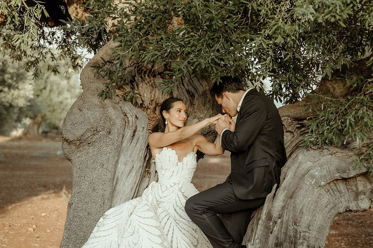 Groom kissing the hand of his bride under a centennial olive tree, filmed by a Puglia Wedding Videographer