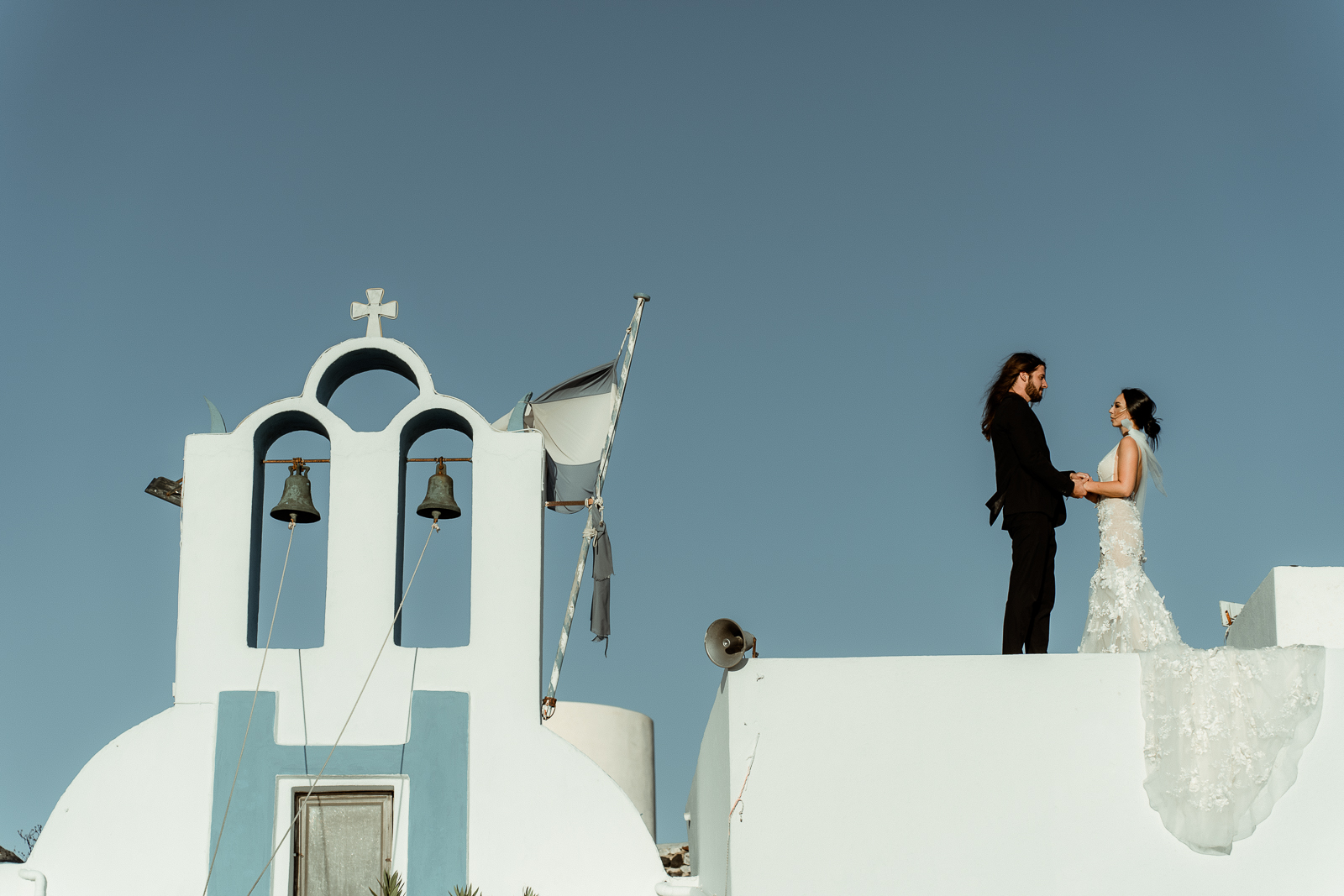 Wedding couple holding hands on top of a white church in Emporeio, filmed by a Santorini Wedding Videographer