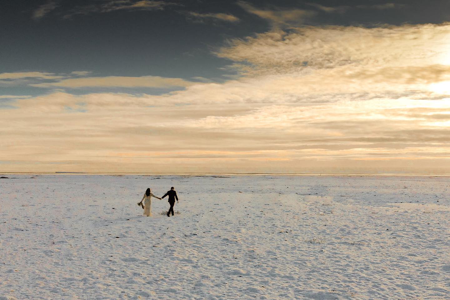 Iceland Elopement Videographer for Adventure & Intentional Celebrations 7 A couple in wedding attire walking on a field full of snow, filmed by an Iceland Elopement Videographer