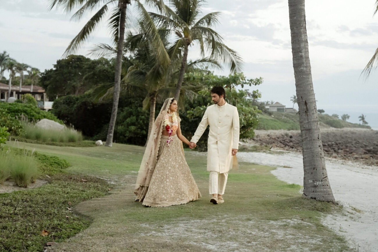 A Couple in Indian Wedding attire walking hand in hand on the beach of Mexico filmed by an Indian Destination Wedding Videographer