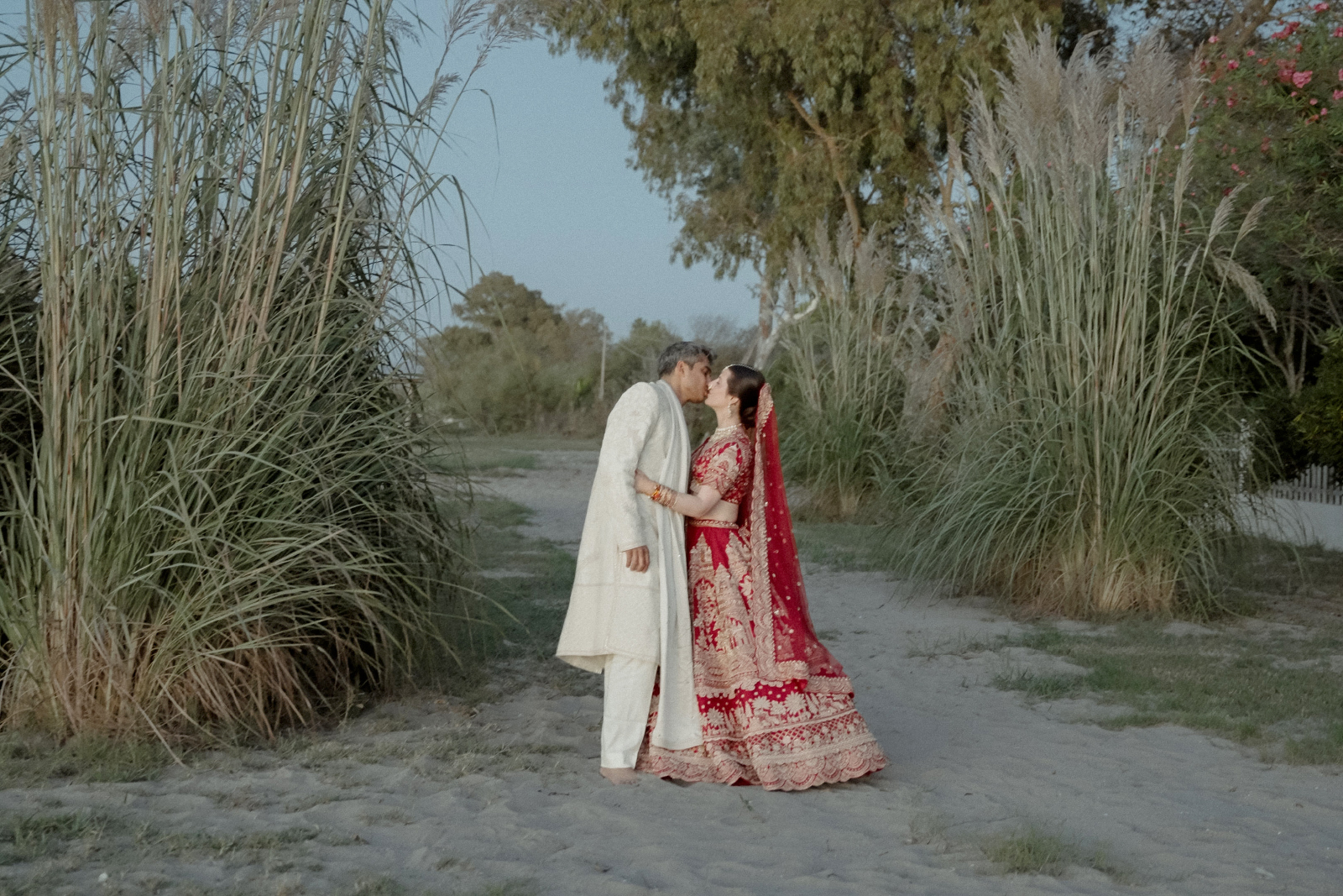Indian Destination Wedding in Corfu at Natura Estate 8 A couple in Indian wedding attire kiss on a beach after their Indian destination wedding in Corfu at Natura Estate