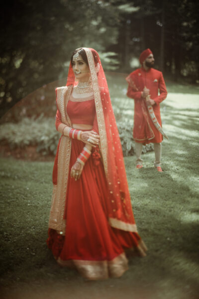 Indian Destination Wedding Videographer 11 Portrait of a bride in the foreground and groom in the background wearing red Indian Wedding attire, filmed by an Indian Destination Wedding Videographer