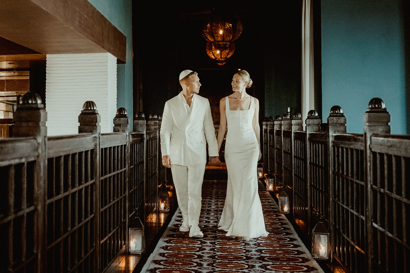 Bride and groom dressed in white walking hand in hand inside the Fairmont Marrakech before their Jewish Wedding Ceremony in Agafay Morocco