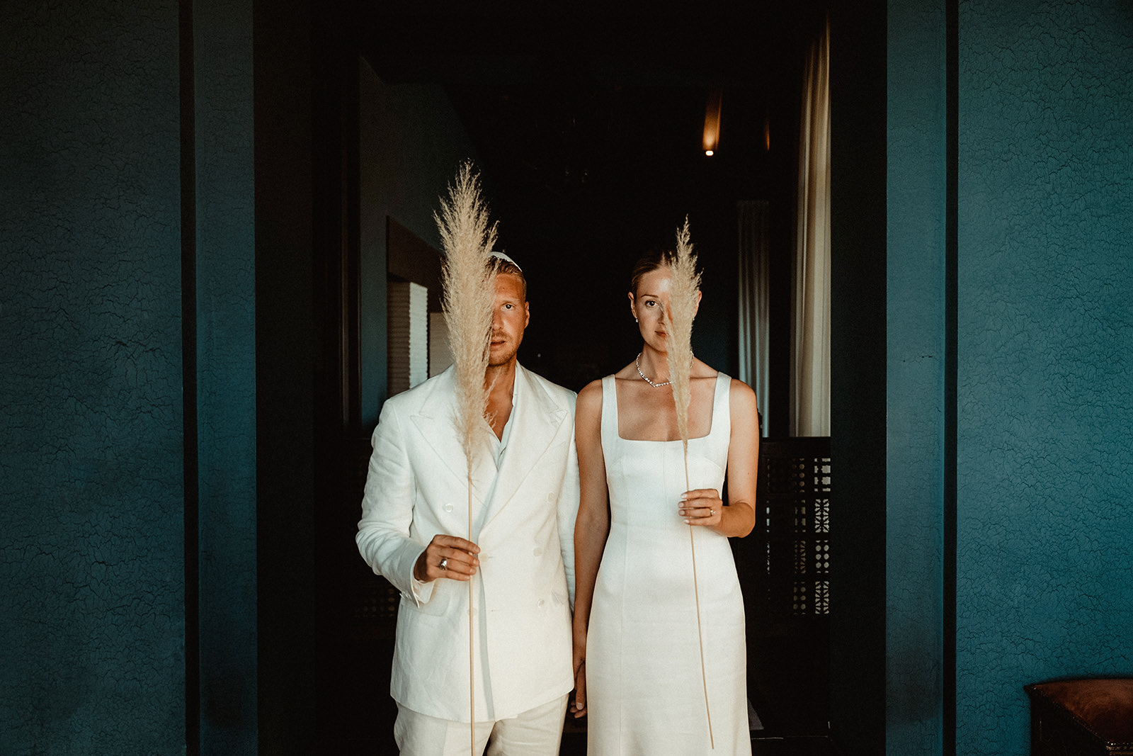 Bride and groom dressed in white and holding pampas inside the Fairmont Marrakech before their Jewish Wedding Ceremony in Agafay Morocco