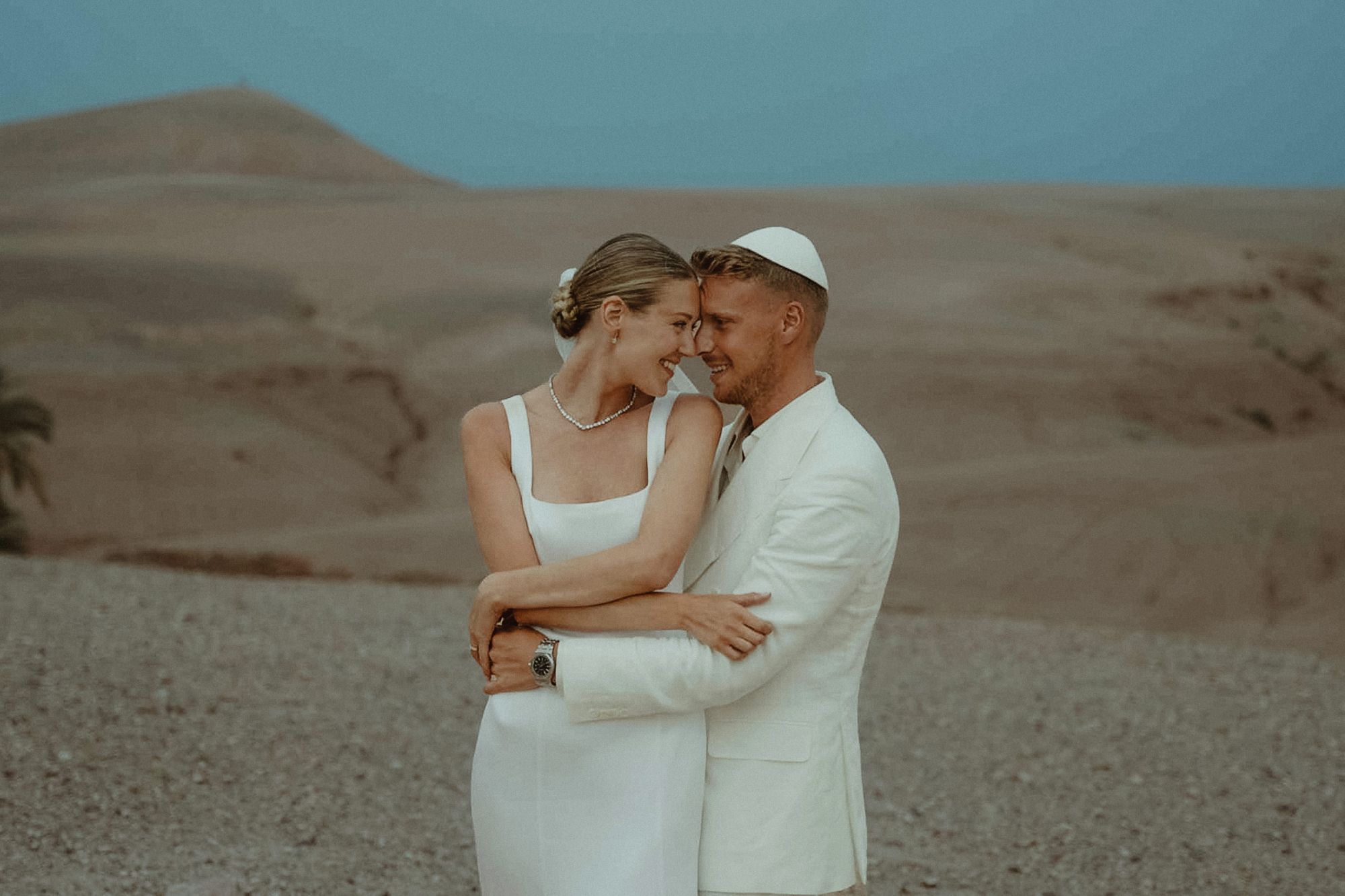 Toronto Wedding Videographer 4 Bride and groom hugging and smiling at each other in the desert after their Marrakech Jewish Wedding Ceremony at Scarabeo Camp in Morocco