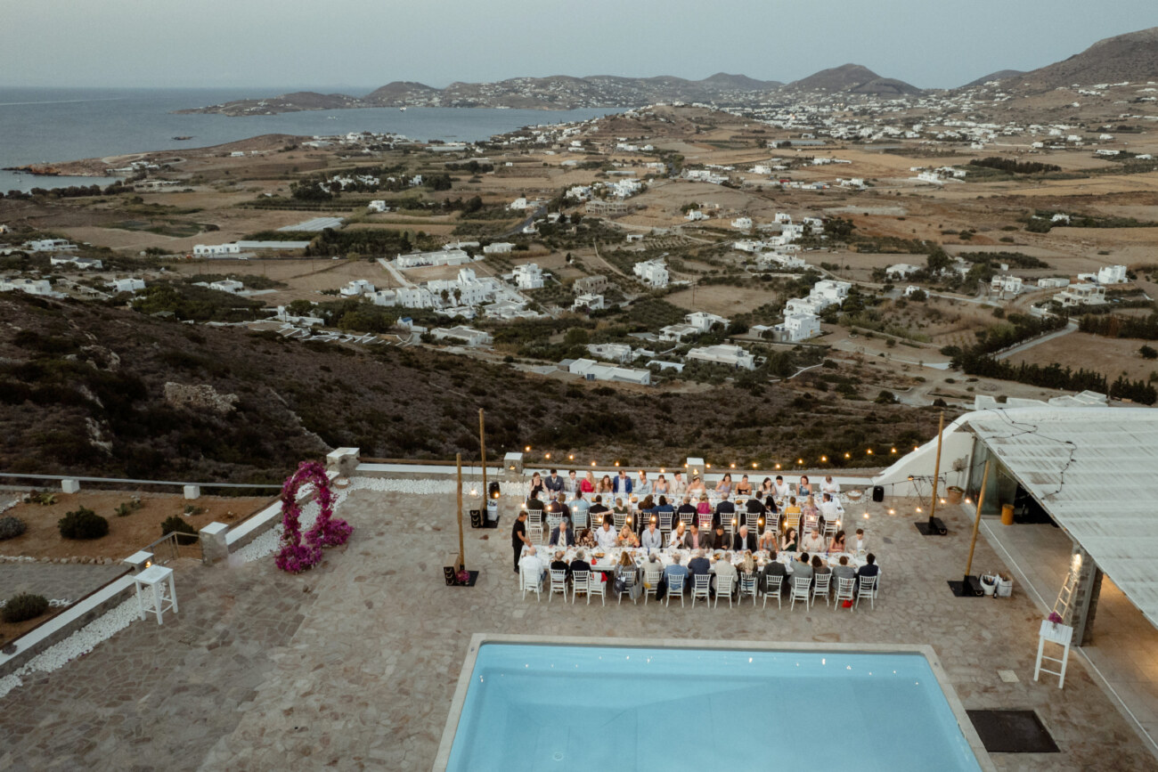 How to Plan a Destination Wedding in Greece, What to Know Before You Begin 2 A wedding dinner setup with two rows of tables in a private villa in Paros Greece with a background view to the sea