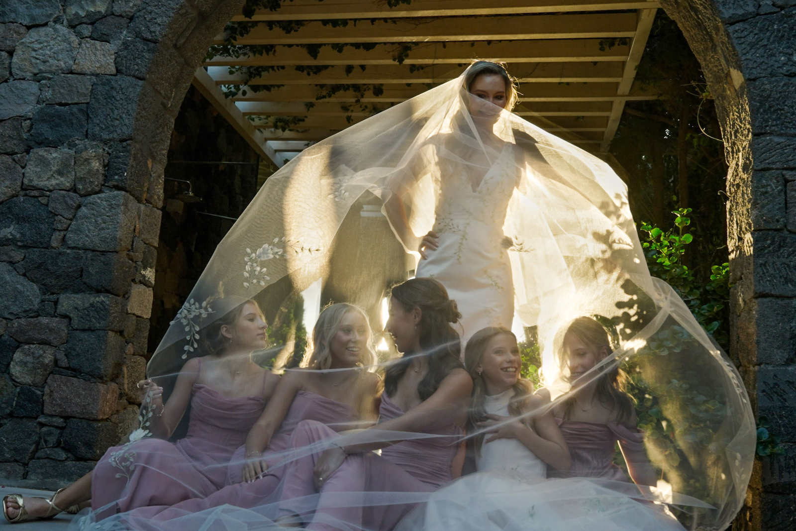 Children sitting and smiling under the bridal veil of their mother at Canaves Oia Santorini