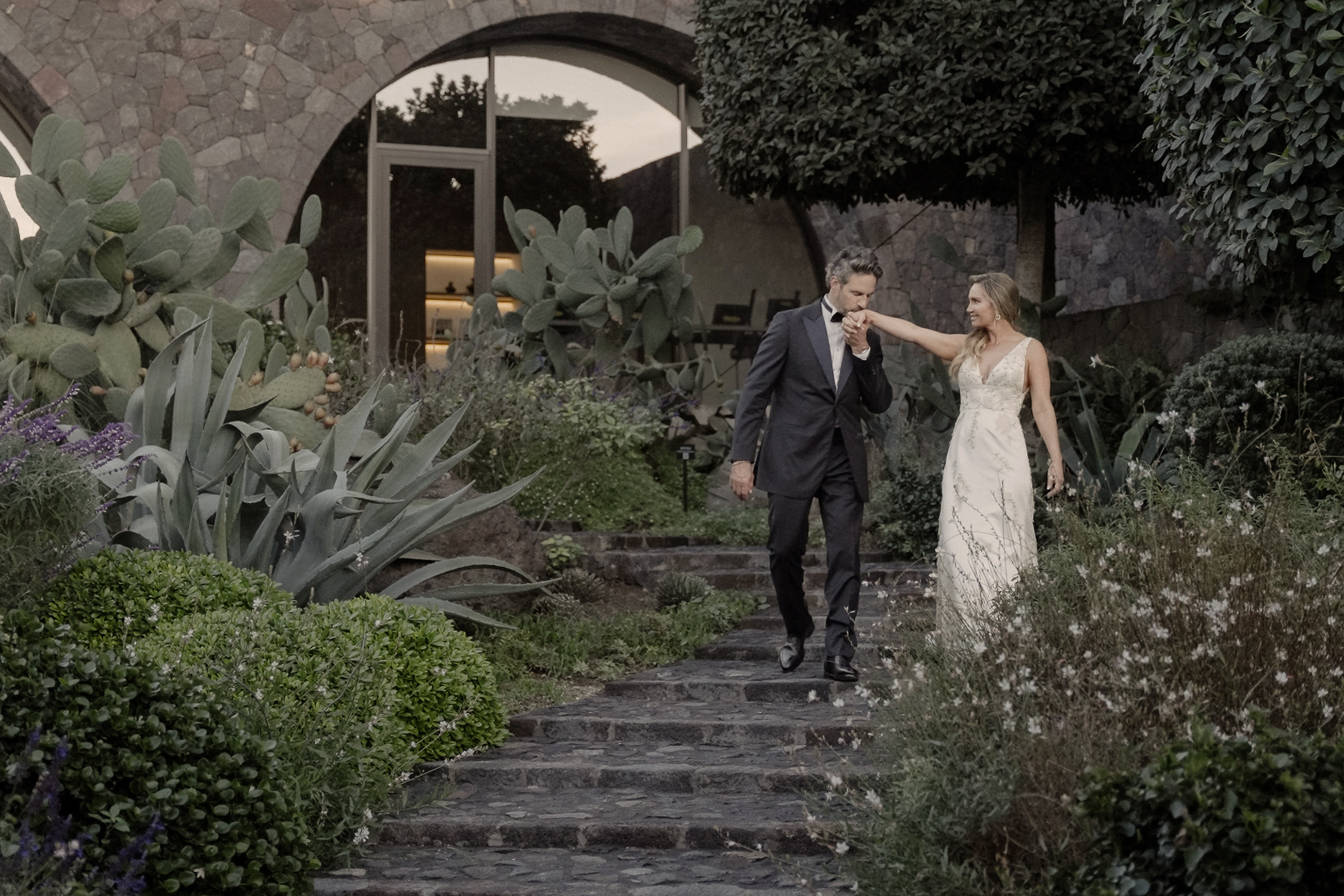 Groom kissing the hand of his bride in a garden after their intimate Santorini Wedding at Canaves Oia