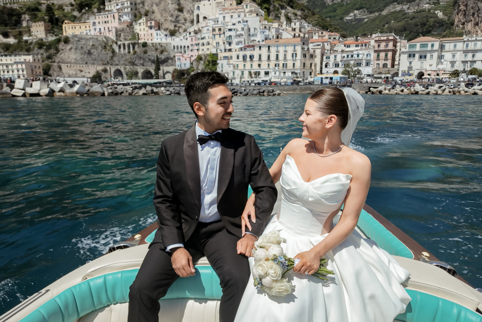 Bride and groom on a vintage Riva boat tour with Amalfi in the background after their Belmond Caruso Wedding in Ravello